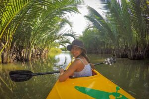 Smiling traveler kayaking through a tunnel of nipa palms in the Hoi An mangrove forest