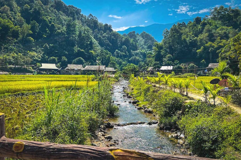 A stream running through a hidden valley with rice fields and jungle mountains and Kho Muong Village in the background