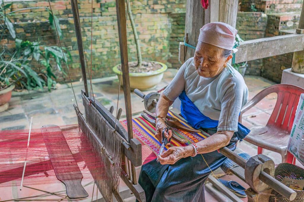 A White Tay ethnic minority woman in traditional dress is weaving at a local workshop in Lac Village