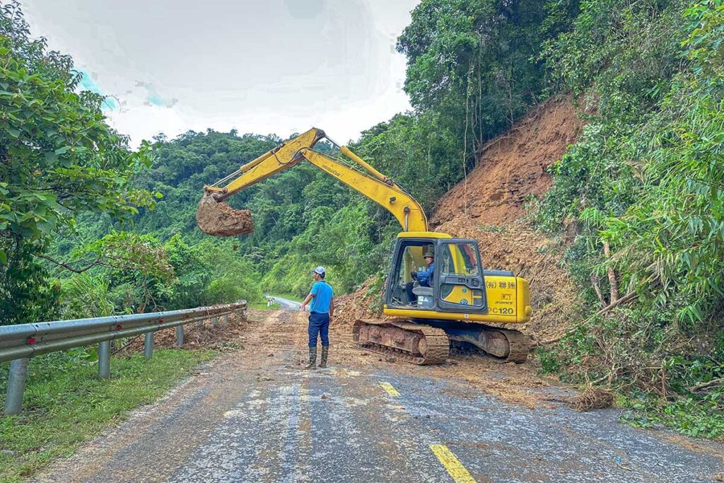 An excavator clearing a landslide from a mountain road in Vietnam