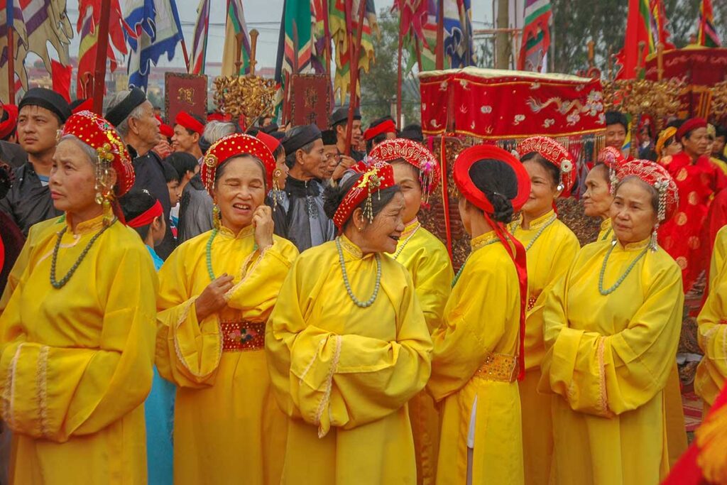 Woman traditionally dressed in bright yellow clothes and red headbands are walking in a parade down the street of Bac Ninh during Lim Festival 