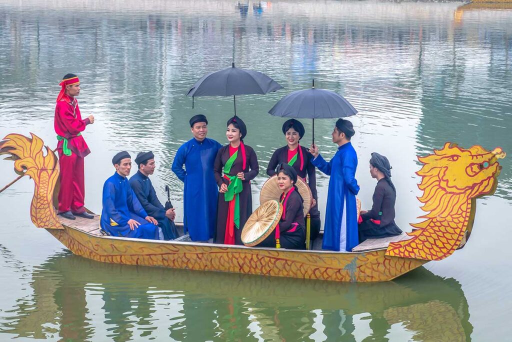 A group of traditionally dressed people on a small dragon boat doing a Quan Ho Singing Performance during the Lim Festival in Bac Ninh