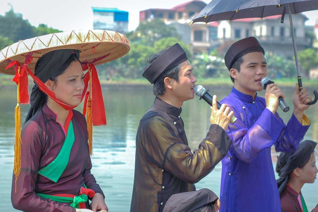 A man in traditional clothes is singing Quan Ho with a microphone while on a boat during Lim Festival in Bac Ninh