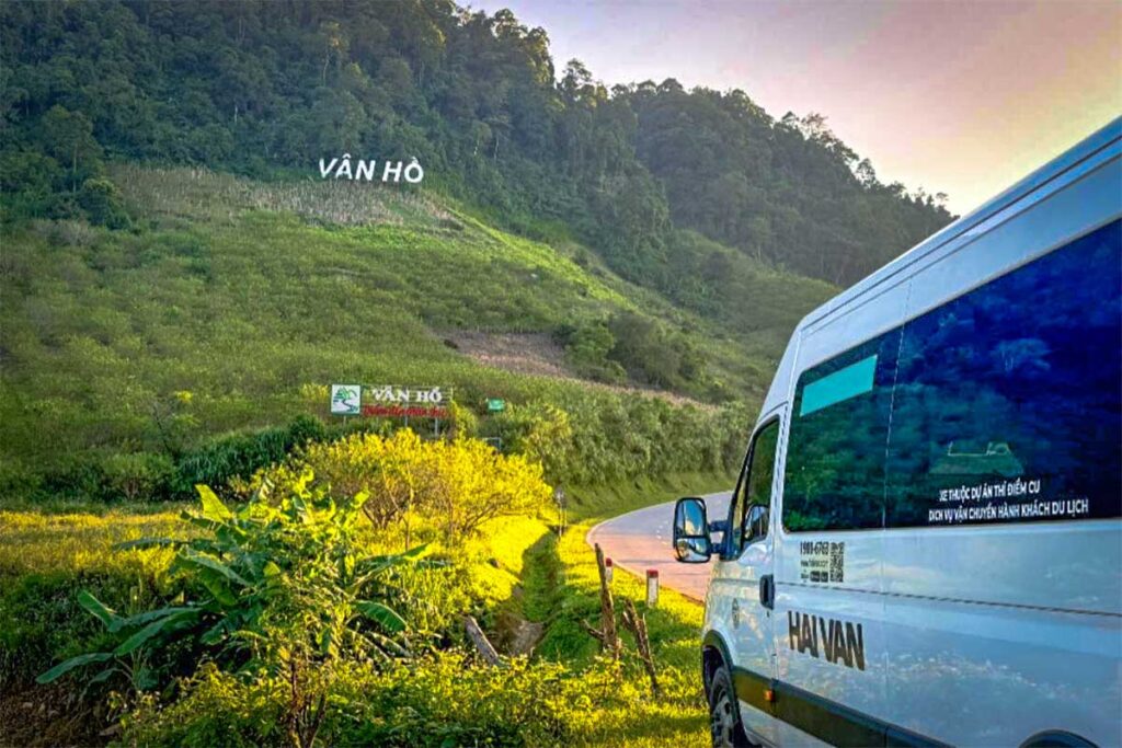 A limousine van from Hanoi is parked along the road at a sign on the hill saying Van Ho
