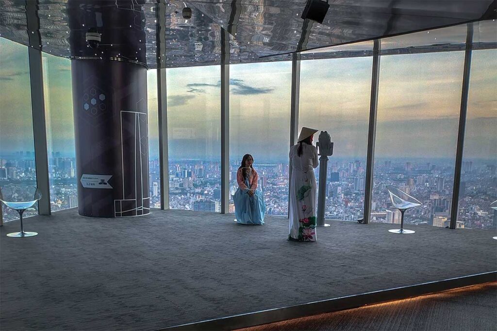 Two girls using fixed binoculars to see the streets and houses of Hanoi below at Lotte Observation Deck