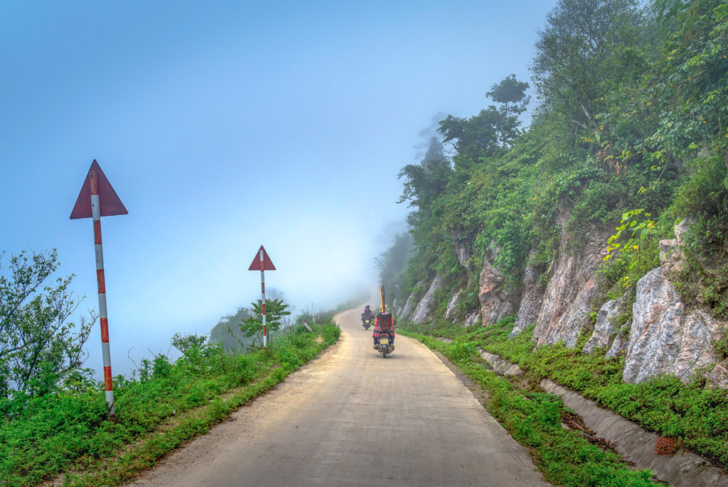 People driving the Mai Chau Loop by scooter on a mountain road during cloudy conditions
