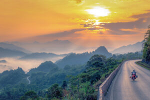 A traveller driving on a motorbike over a high mountain pass with stunning mountain views during sunset while following the Mai Chau Loop