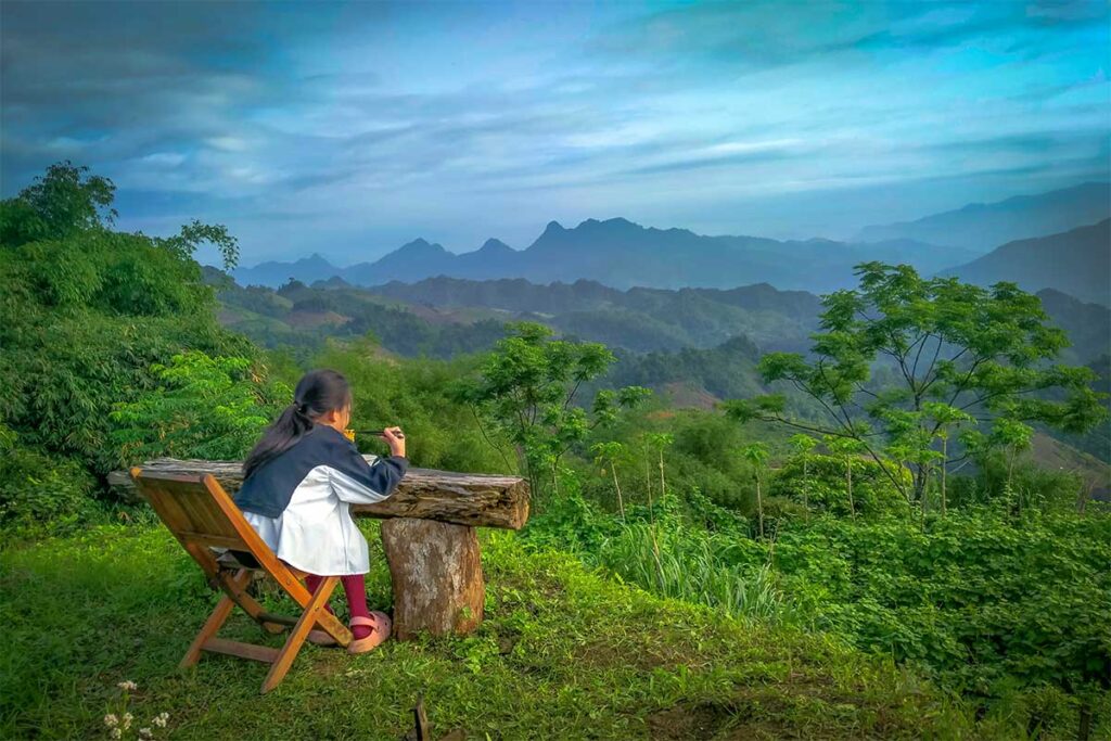 A girl eating food on a foldable chair with stunning mountain and jungle views at May Do