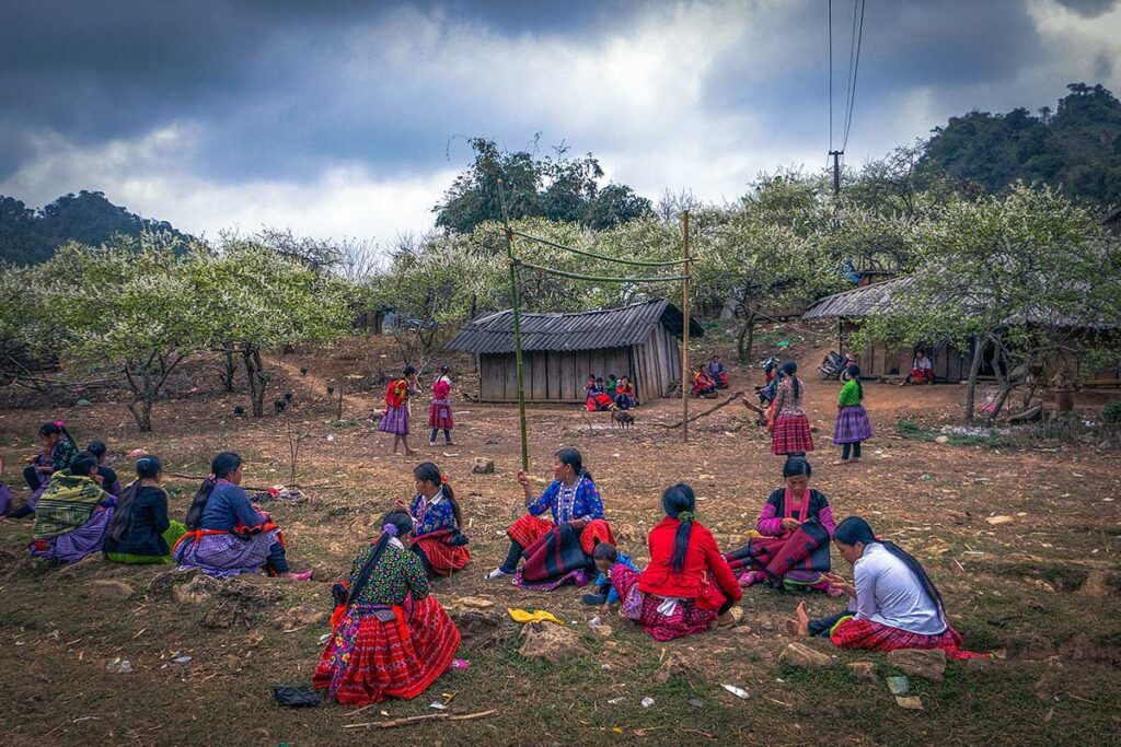 A group of ethnic minority woman in colorful traditional clothes sitting on the ground at a local village near Moc Chau