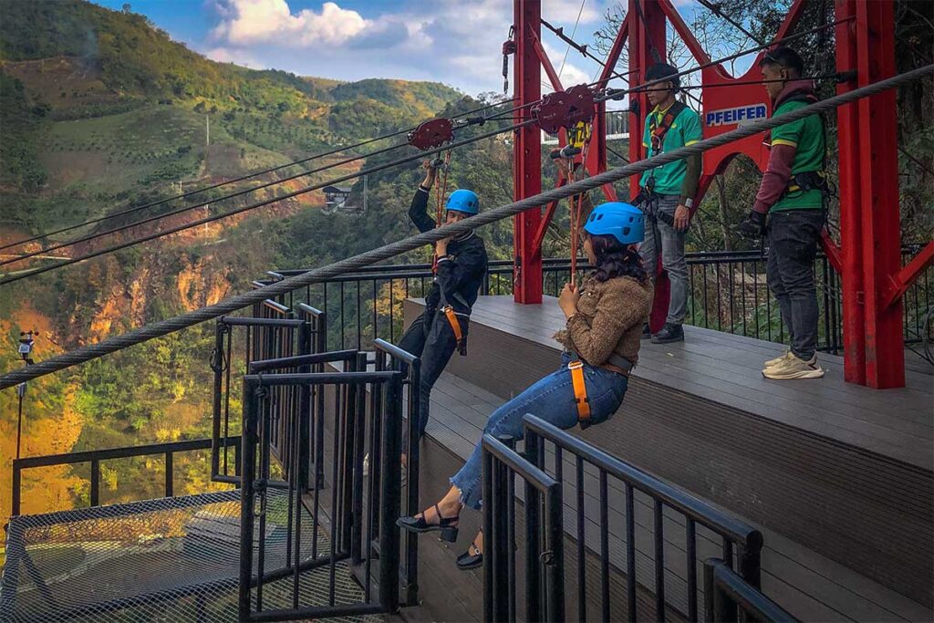 Two people are hanging at the starting point of the zipline in Moc Chau near the Glass bridge