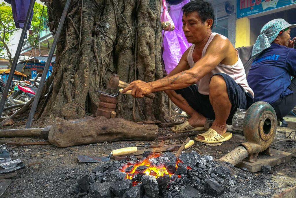 A man working next to a tree with small open fire in the village of Nom in Hung Yen