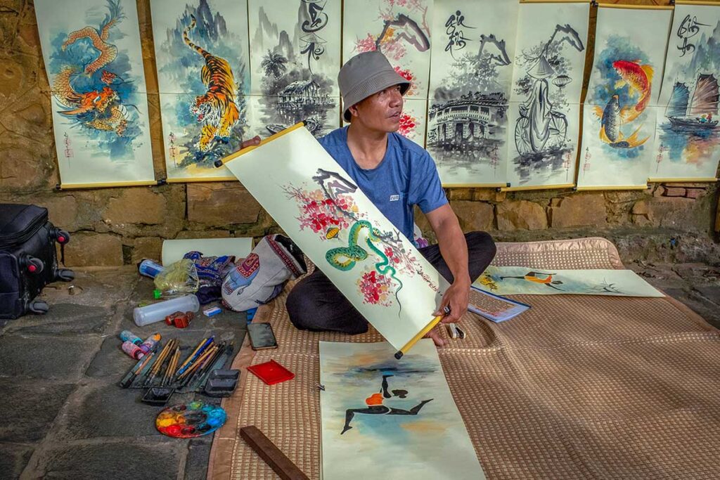 A man showing his painting in style of Vietnamese art with different other paintings behind him in Hanoi