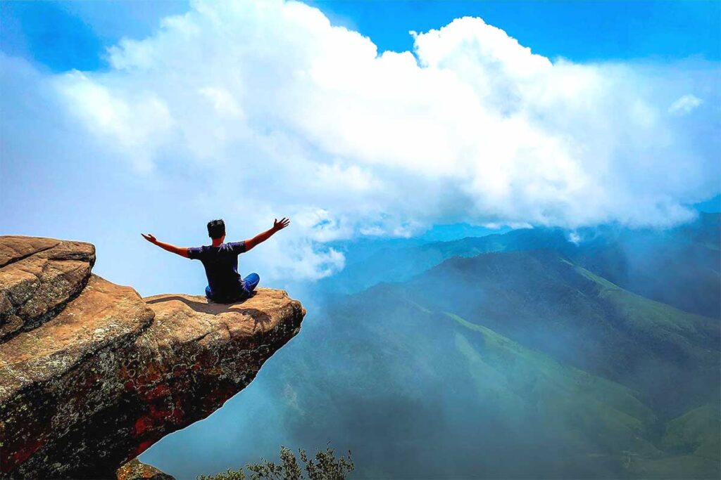 A man sitting on a rock that sticks out so it looks a very dangerous place to sit