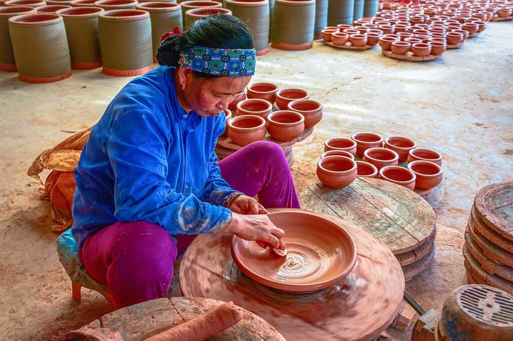 A local woman is using her hands to shape a clay bowl at Phu Lang Pottery Village