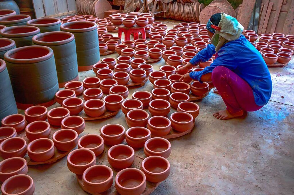 A woman sitting next to many just made clay pots at Phu Lang Pottery Village