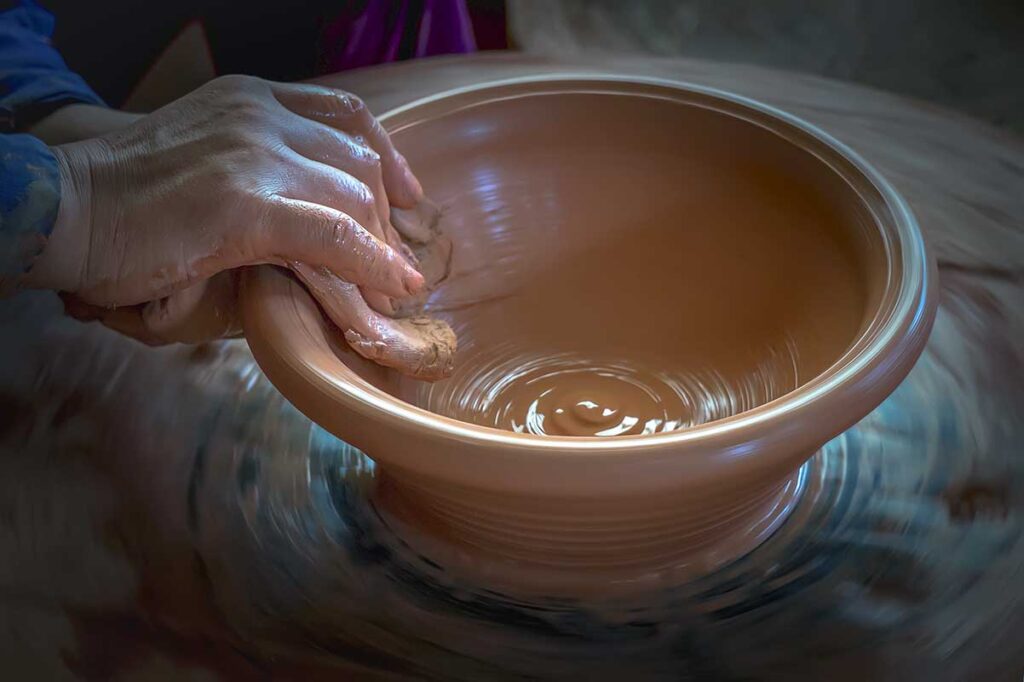 A hand on a spinning wheel making a bowl out of clay at Phu Lang Pottery Village