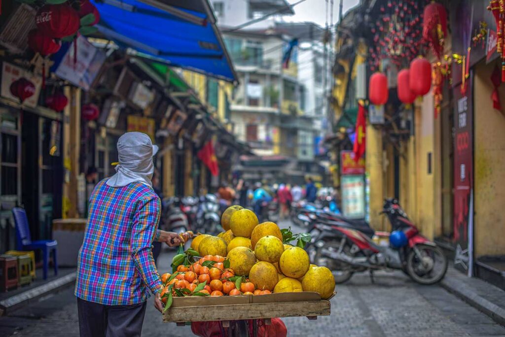 A fruit seller on a bicycle walking through Ta Hien street during the day in Hanoi Old Quarter