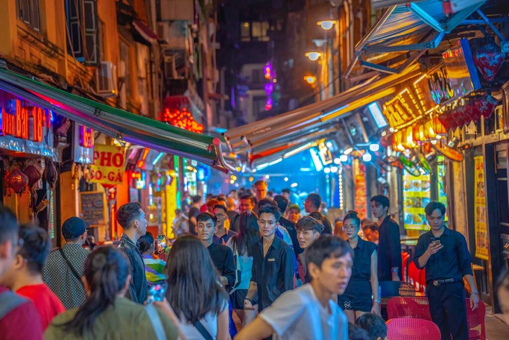 A busy Ta Hien Street at night, also called Bia Hoi street, with lots of locals and tourists walking through the street full of bars in the Old Quarter