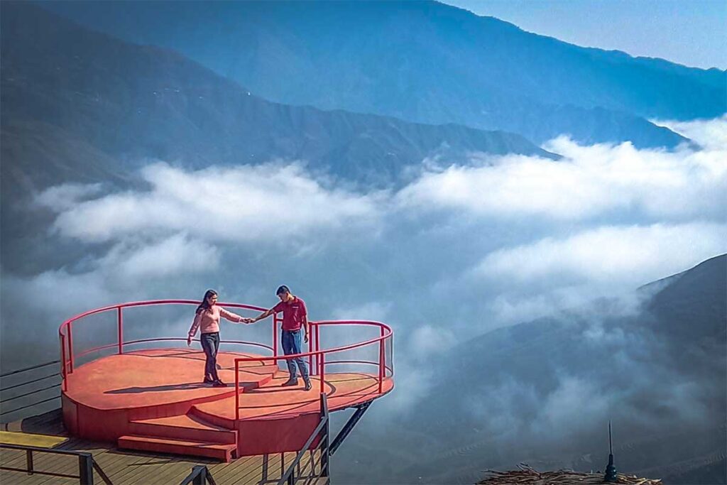 A heart shaped viewing platform used for cloud hunting with a couple holding hands that is part of a cafe overlooking the mountains of Ta Xua 