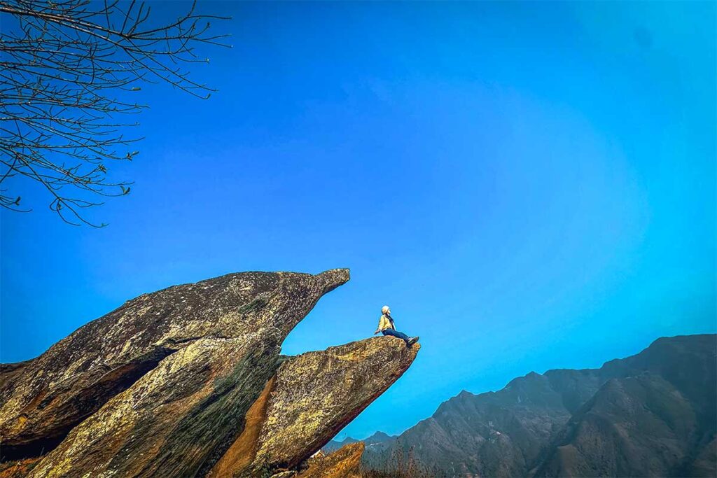 A woman sitting on a rock them looks a lot like the beak of a dolphin, nicknamed Dolphin Beak Rock of Ta Xua