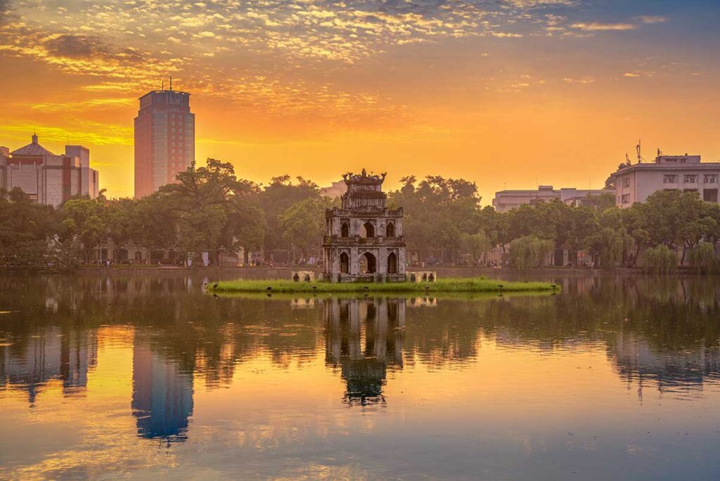 The Turtle Tower during golden sunset with lights, the tower and buildings surrounding Hoan Kiem Lake reflecting on the water