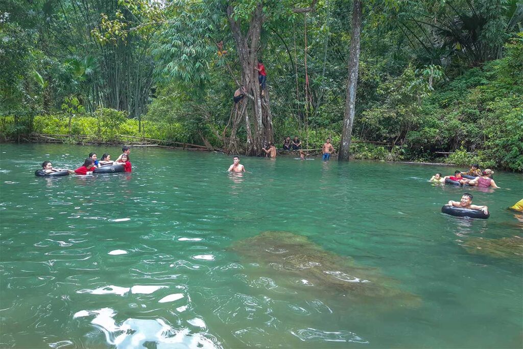 Locals swimming and floating in a stream surrounded by forest inside Xuan Son National Park