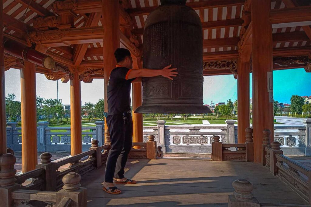 A man putting his arms around a giant bell to show its size at Xuong Giang Ancient Citadel
