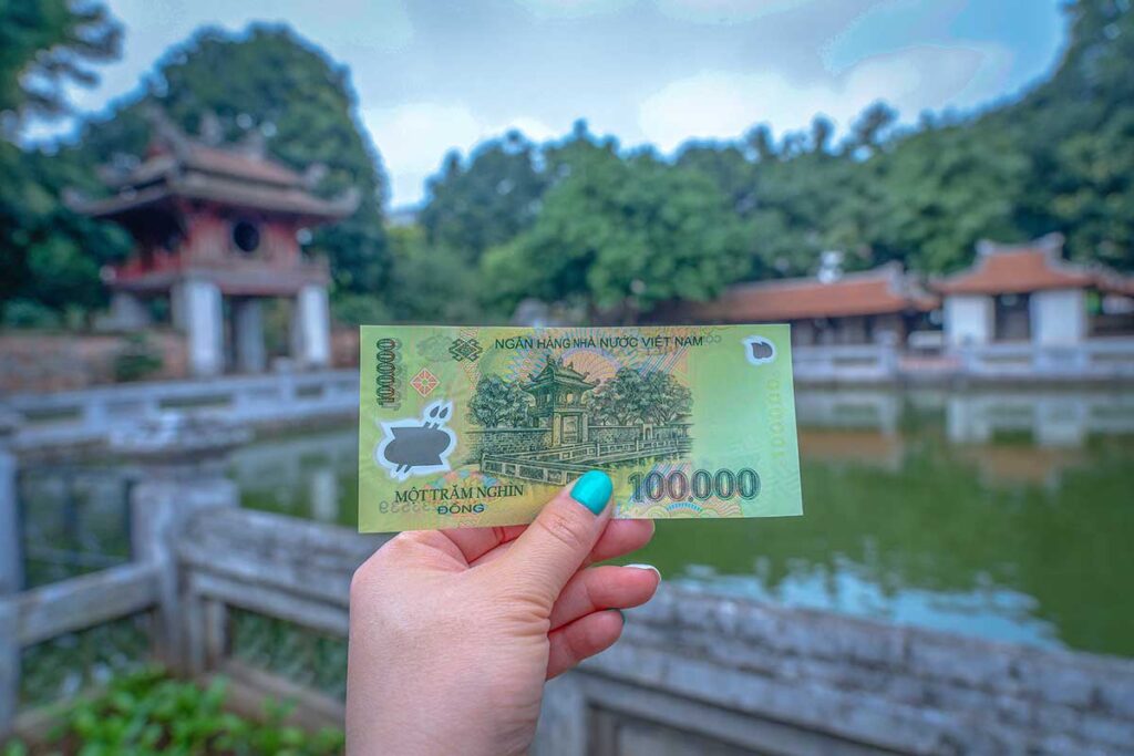 Vietnam 100,000 dong banknote in woman hand with in the background the Khue Van Pavilion which is also displayed on the reverse side of the bill. At the ancient Vietnamese fortress of Van Mieu or Temple Of Literature