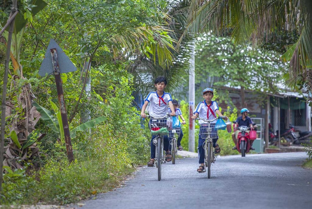 School children cycling over a countryside lane between the trees on An Binh Island - Vinh Long Province