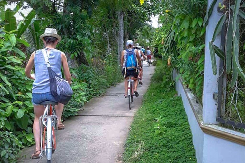 Tourist are cycling on a narrow countryside path on An Binh Island in Vinh Long - Part of the Mekong Delta