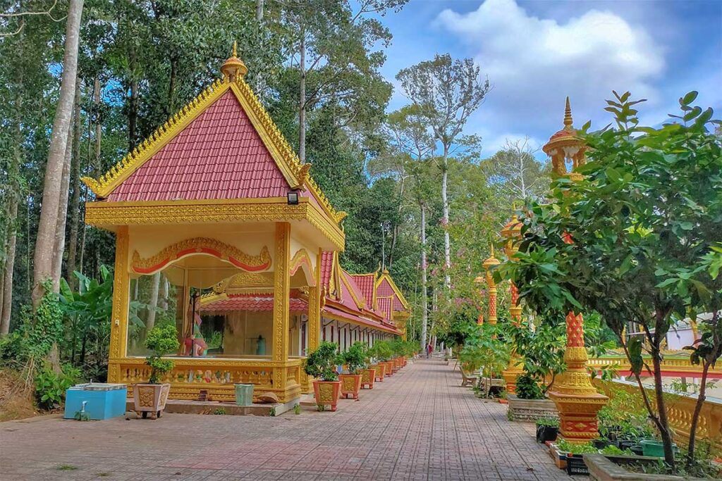 Shaded walkway with golden pavilions and trees inside Ang Pagoda complex in Tra Vinh.