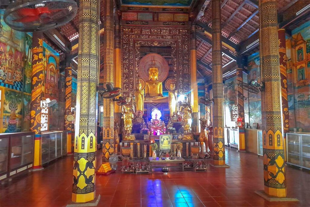 Interior of Ang Pagoda main hall in Tra Vinh with golden Buddha statue, decorated pillars, and murals.