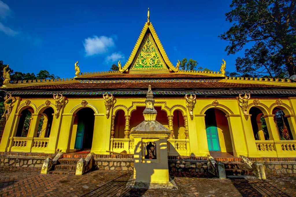 Front view of Ang Pagoda main hall in Tra Vinh with golden Khmer architecture, dragon motifs, and a steep roof under blue sky