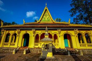 Front view of Ang Pagoda main hall in Tra Vinh with golden Khmer architecture, dragon motifs, and a steep roof under blue sky