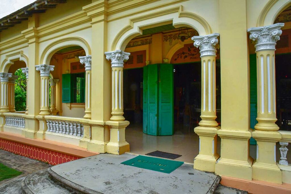 Yellow colonial façade with arched windows and pillars at Ba Duc Ancient House in Cai Be