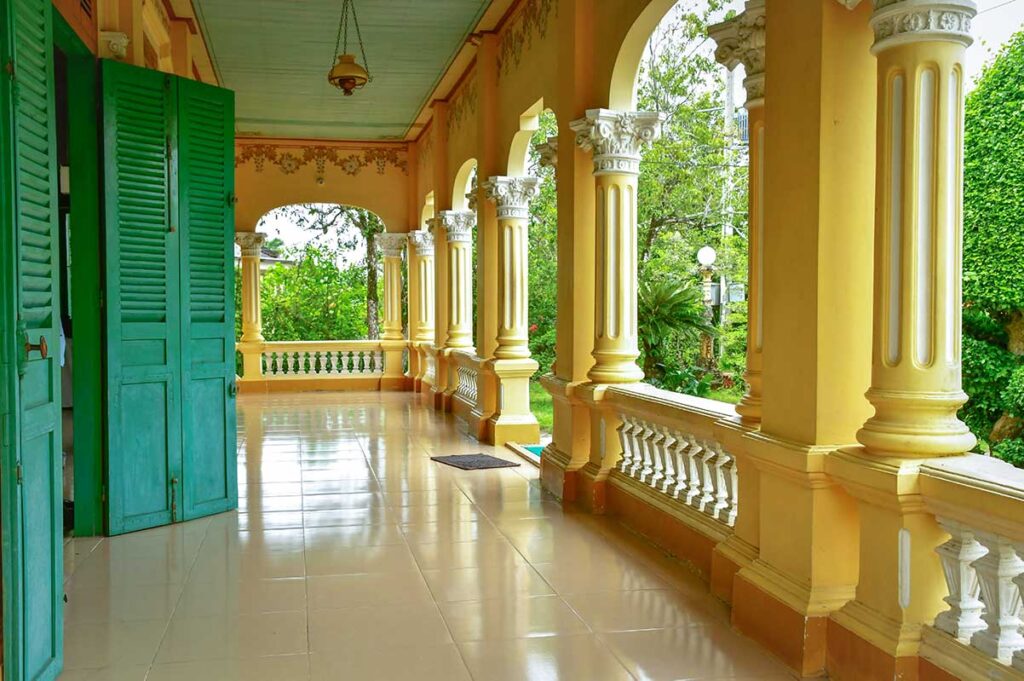 Colonial-style balcony with green shutters and ornate columns at Ba Duc Ancient House, Cai Be