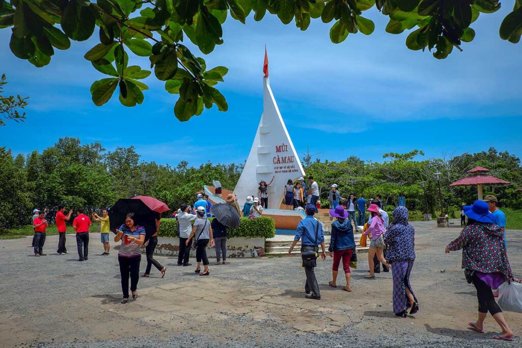 Domestic tourists walking along a monument of Cape Ca Mau and taking pictures
