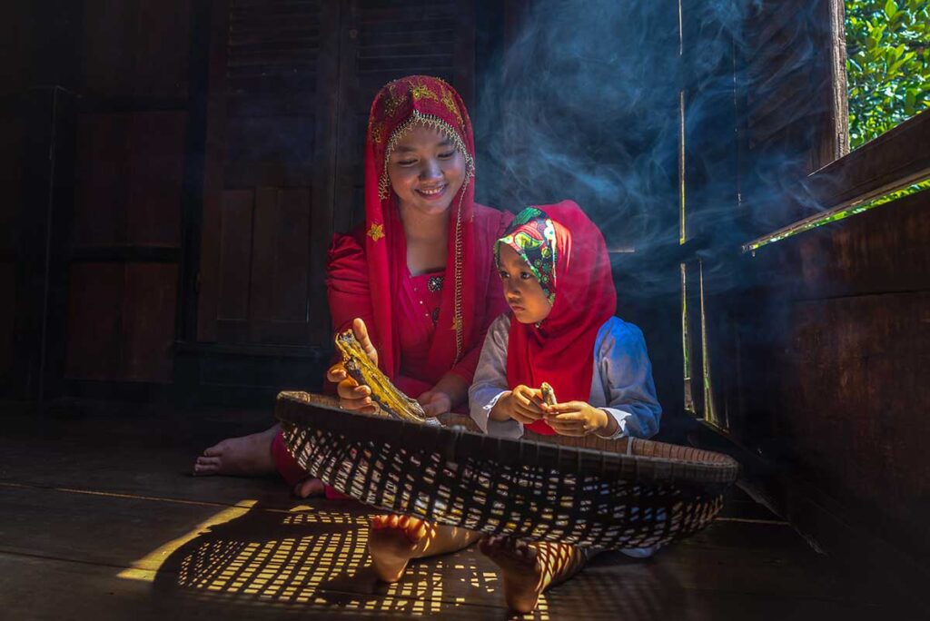 A muslim woman and her child sitting in their stilt house busy preparing dried fish
