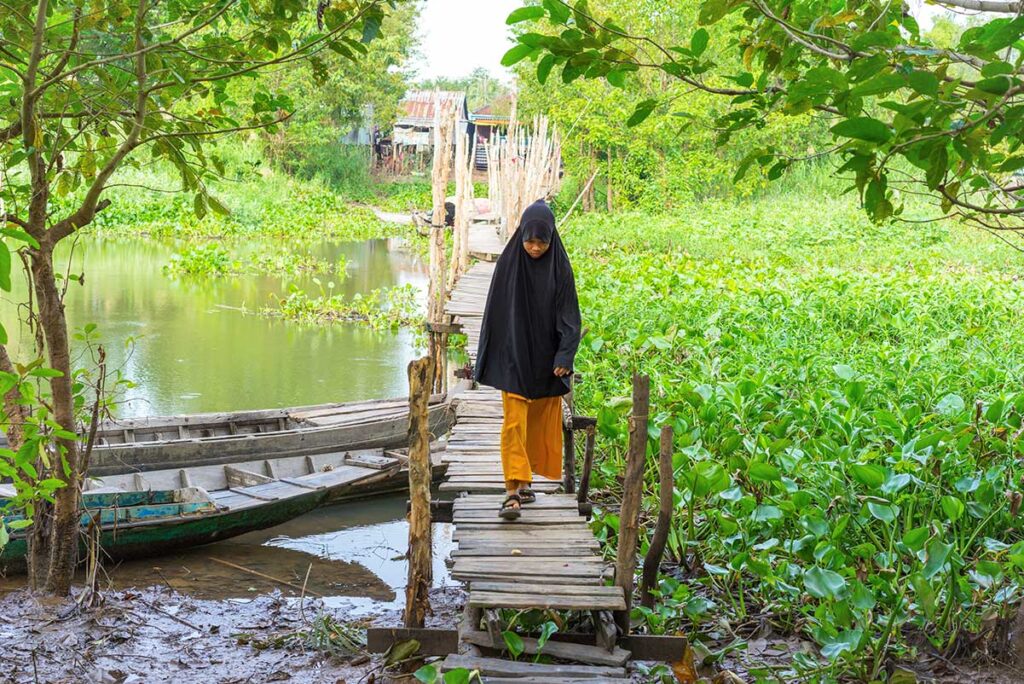 A muslim girl walking over a wooden boardwalk in Chau Giang Cham Village near Chau Doc