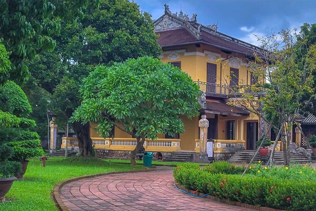 A stone path leading through a small garden with trees and hetches part of Dien Tho Residence