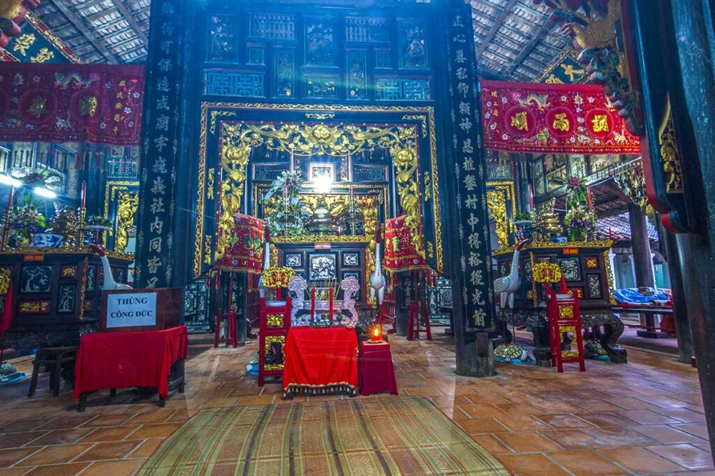 Ornate altar inside Dinh Yen Temple with gilded wood carvings, ancestral worship items, and traditional red and gold decorations