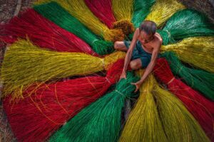 Elderly craftsman arranging bundles of dyed sedge grass into circular patterns at Dinh Yen Mat Weaving Village