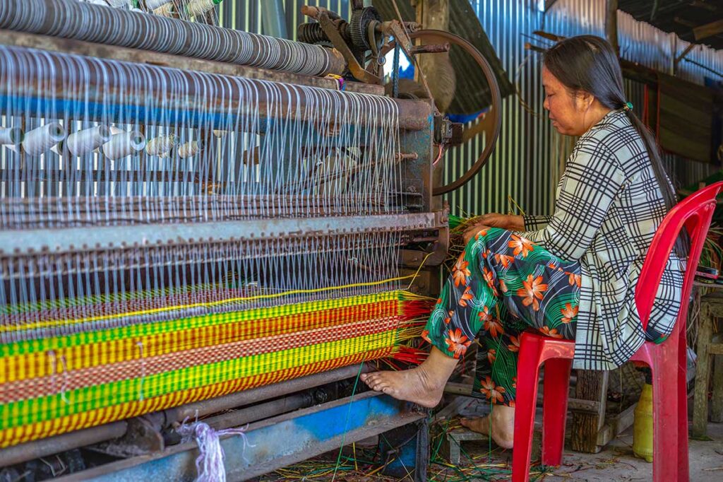 A woman weaving a colorful sedge mat on a mechanical loom at Dinh Yen Mat Weaving Village in Dong Thap, Vietnam
