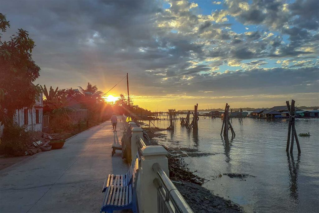 Sunset view along the embankment walkway of Dragon Island (Tân Long), with fishing structures on the river.
