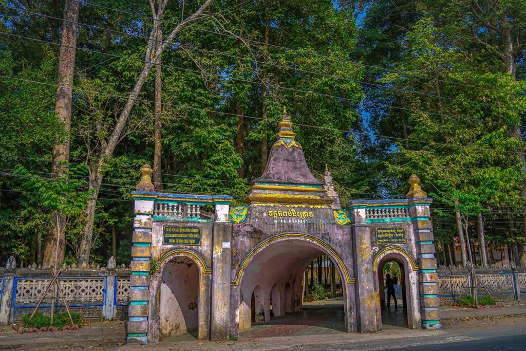 Entrance gate of Hang Pagoda in Tra Vinh, built in a cave-like style with three arched passages surrounded by tall trees.