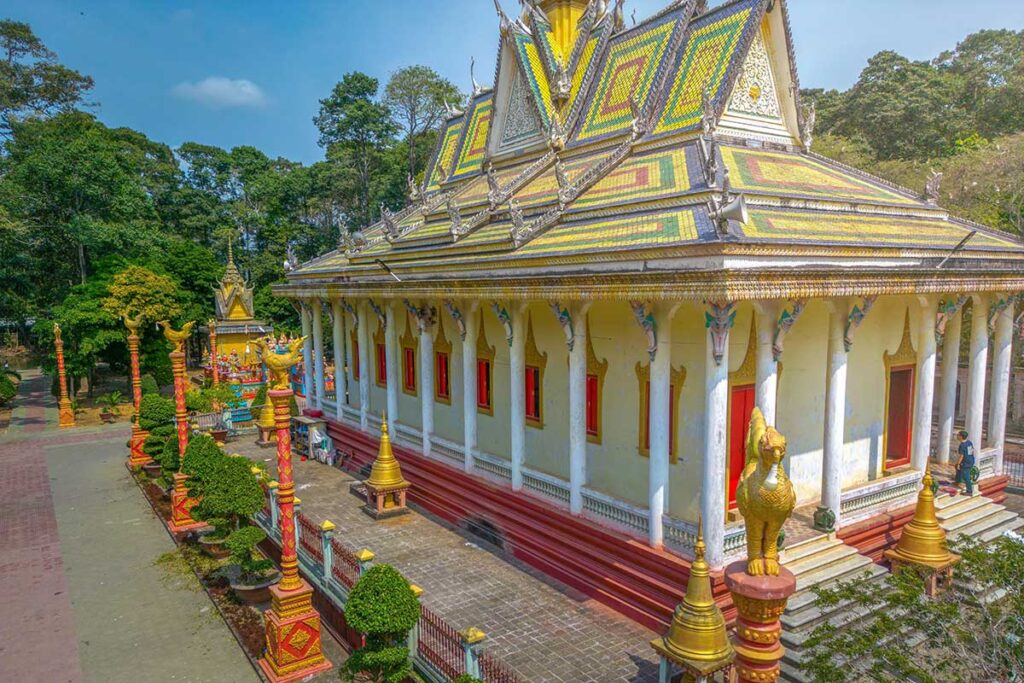 Main hall of Hang Pagoda in Tra Vinh with colorful Khmer-style roof tiles and golden statues along the walkway.