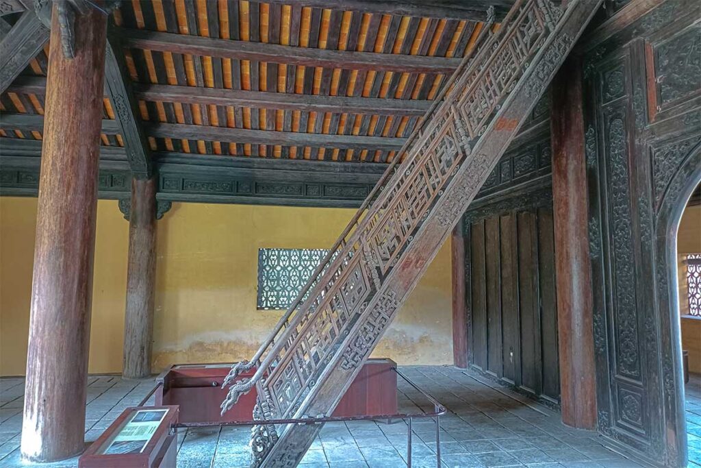 Inside Hien Lam Pavilion, the interior of the first floor with wooden columns and the steep stairs leading to the second floor of the building
