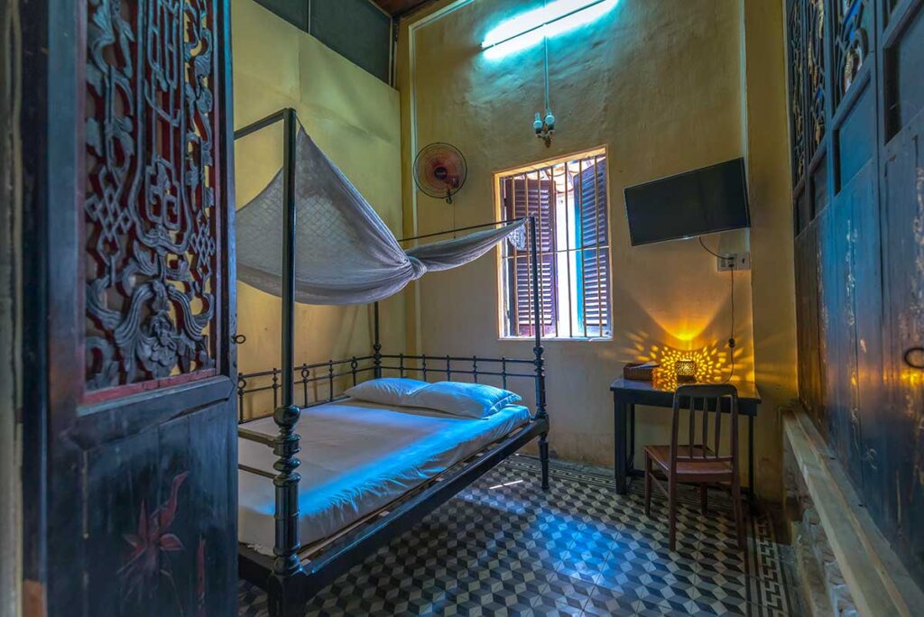 Traditional bedroom with vintage bed, mosquito net, and patterned floor tiles at Huynh Thuy Le Ancient House