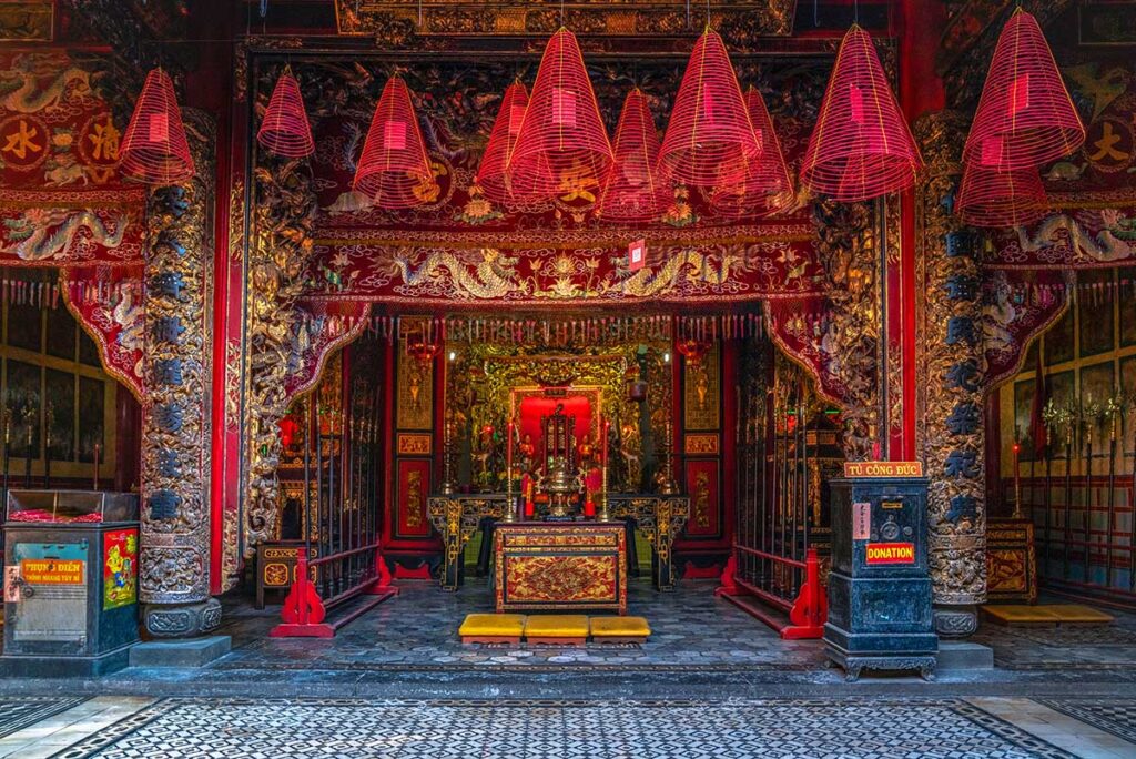 Main altar inside Kien An Cung Temple decorated with golden carvings, red banners, and spiral incense coils