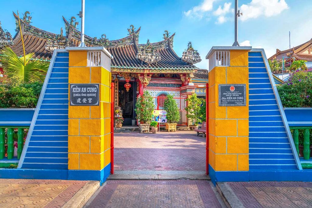 Entrance gate of Kien An Cung Temple in Sa Dec with yellow and blue walls and view of the ornate pagoda